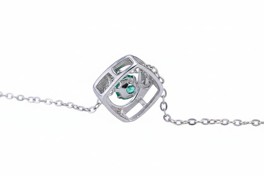 Silver necklace with a cube pendant featuring a green gemstone on a white background